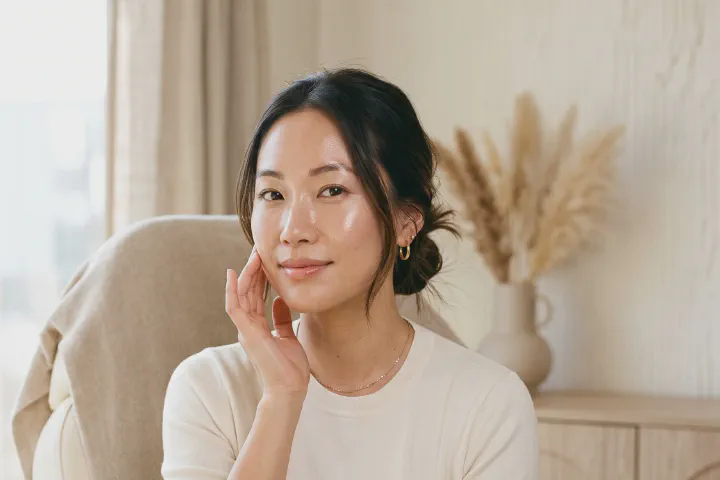 Woman with dewy, healthy-looking skin touching her cheek in a sunlit treatment room at Beautiful Body and Beyond in Corona, CA