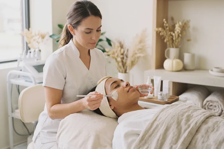 Aesthetician applying a peel solution with a soft fan brush to the cheek of a reclined client at Beautiful Body and Beyond in Corona, CA